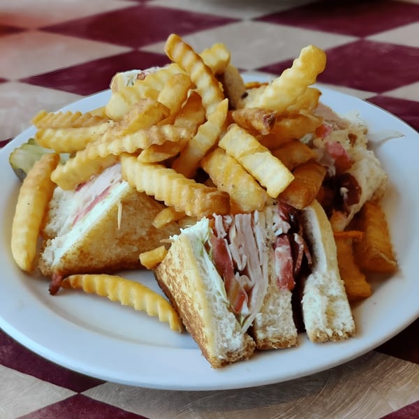 A club sandwich with turkey, bacon, lettuce, and tomato, served with crinkle-cut fries.