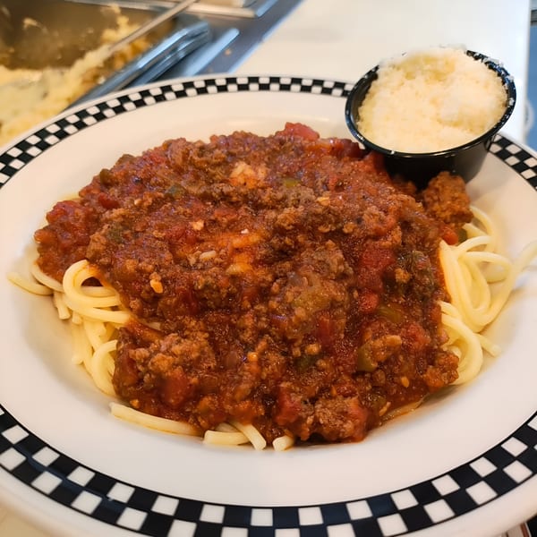 Spaghetti with meat sauce and a side of grated Parmesan cheese on a checkered plate.