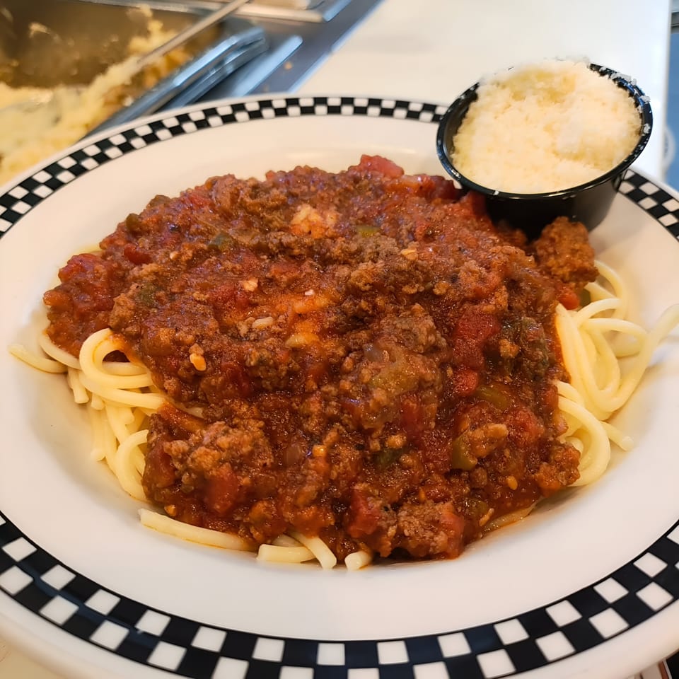 Spaghetti with meat sauce and a side of grated Parmesan cheese on a checkered plate.