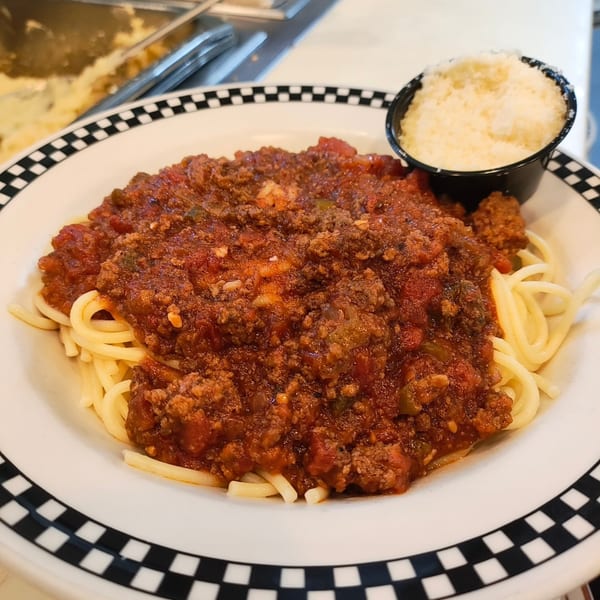 Spaghetti with meat sauce and a side of grated Parmesan cheese on a checkered plate.