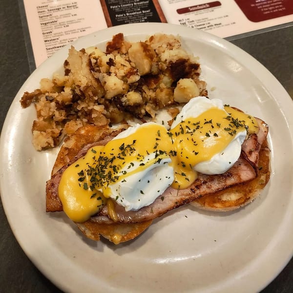 Pete's Restaurant & Coffee Shop's Eggs Benedict with crispy home fries on a white plate.