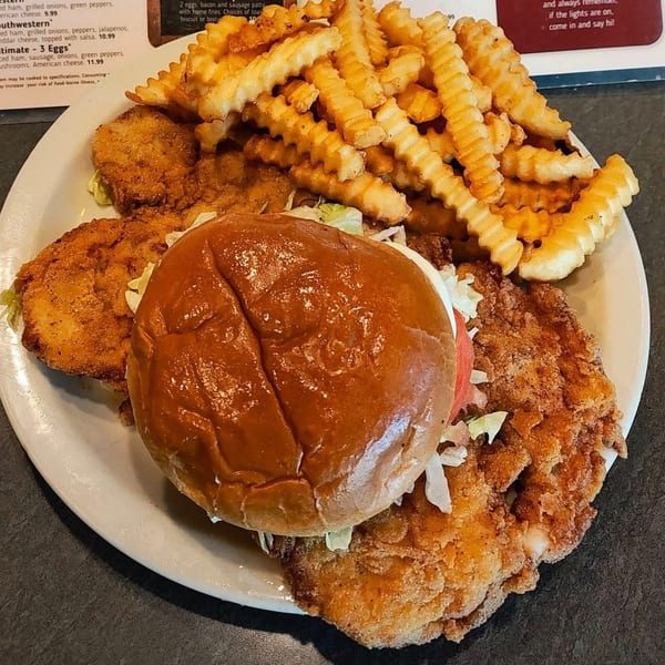 A fried chicken sandwich with lettuce and tomato, served with crinkle-cut fries and extra fried chicken.